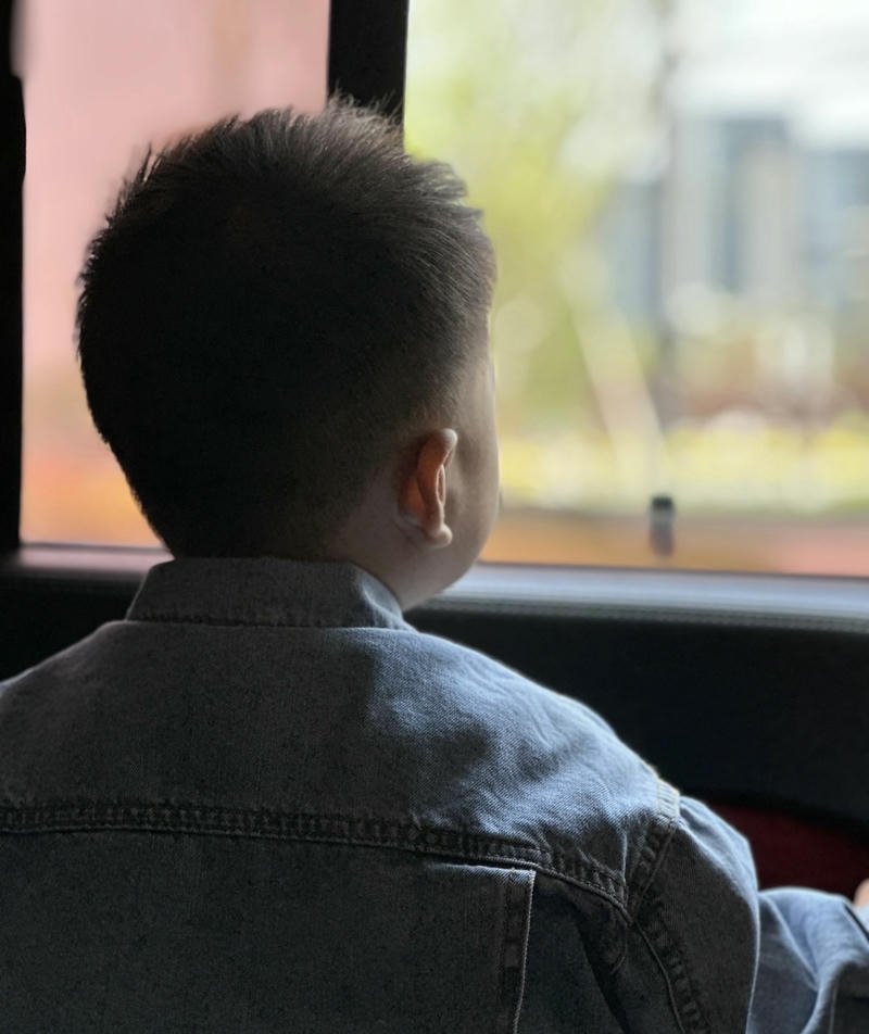 Dáng cậu bé đứng cạnh cửa sổ phòng khách nhìn từ sau